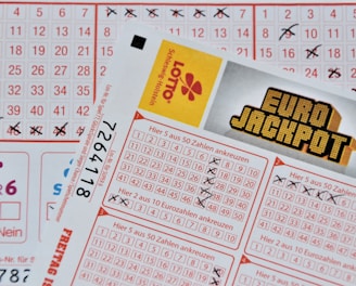Three lottery tickets are displayed, including Eurojackpot and Super 6. Various numbers are marked on the tickets, with some crossed out and others checked. The Eurojackpot ticket is partially visible with the logo prominently displayed, and a ticket number is visible on one of the tickets.